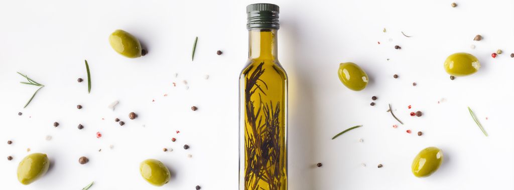A glass bottle of herb-infused olive oil surrounded by fresh olives.