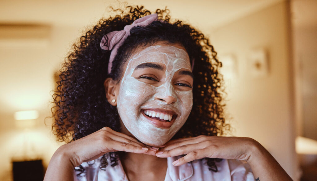 A woman smiling with an exfoliating skin treatment on her face.