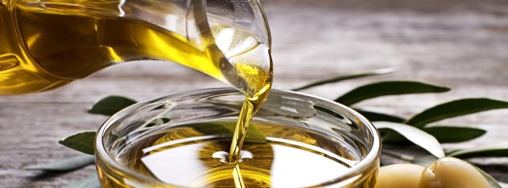 Olive oil being poured from a decanter into a clear glass bowl.