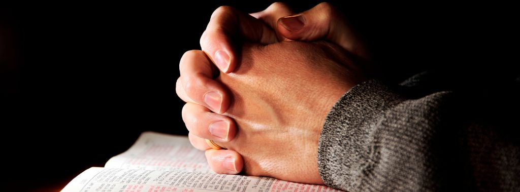 Hands clasped in prayer over Bible.