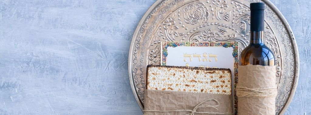 An ornate metal plate with matzah and Passover haggadah against a blue background as a Passover seder feast.
