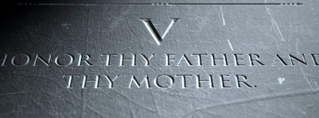 Stone carving of the Fifth Commandment, reading honor thy father and thy mother.