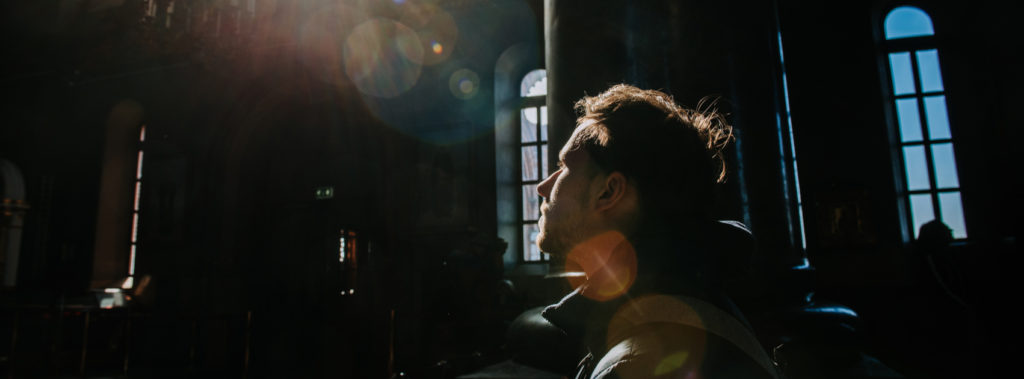 Man sitting in dark church praying for a way to live in hope.