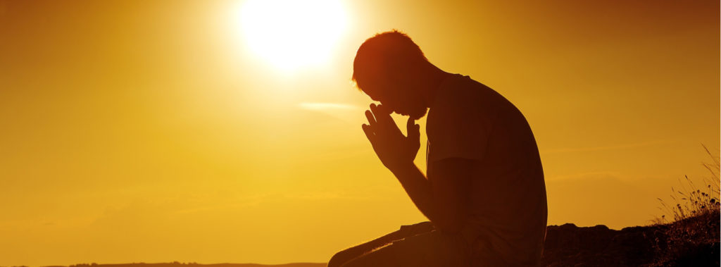 Man sitting on hill under sun praying in expectation.
