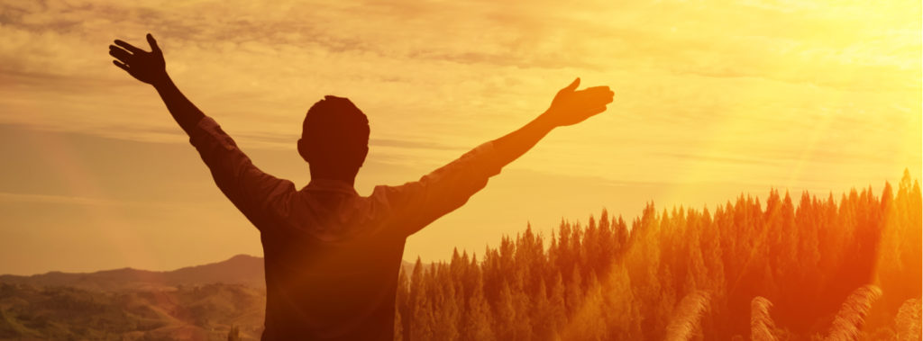 Man raising his hands to the sky in the forest, thanking God.