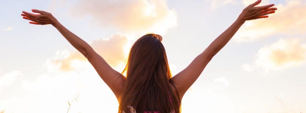 Woman raising arms to sky and living a life of gratitude.