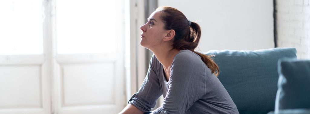 Upset woman sitting on couch, experiencing the effects of being out of spiritual alignment.