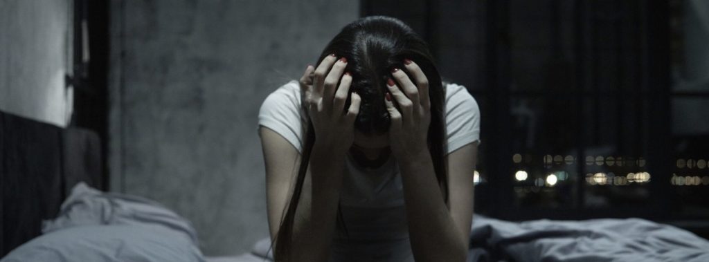 Woman sitting on bed with head in hands, feeling defeated and needing restoration in God.