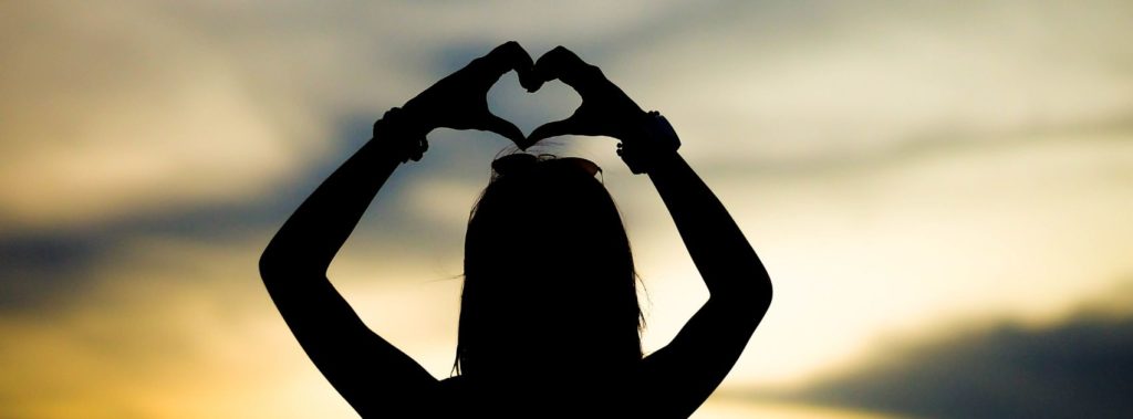 Woman silhouette demonstrating grateful heart by raising hands in shape of heart.