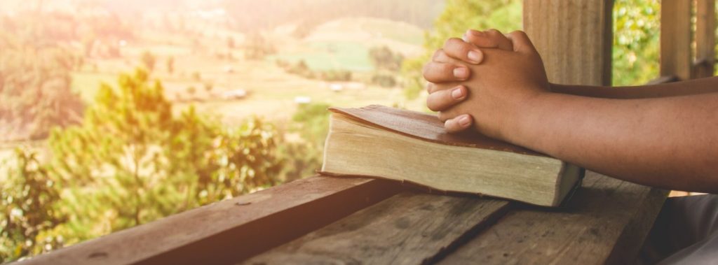 Man praying at window overlooking landscape.