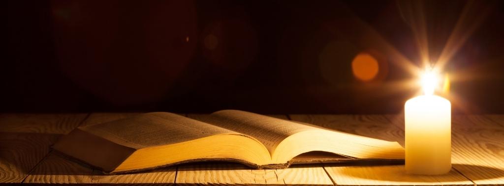 An open Bible on table near the light of a candle.