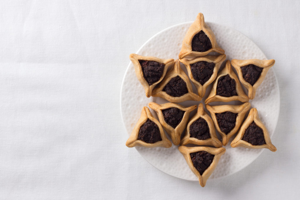 Overhead view of a plate of hamantaschen cookies, triangular cookies with poppy seeds.

