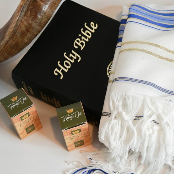 Two bottles of The King’s Oil Holy Anointing Oil® on a table with a shofar, Bible, and tallit.